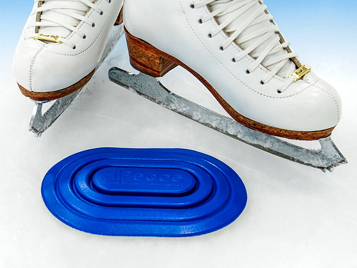 Blue LiveKühn PeacePad on a skating rink in front of a pair of white ice skates