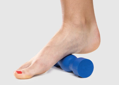 Woman rolling her foot on a blue Swede-O plantar F3 foot roller made from blue Sorbothane material