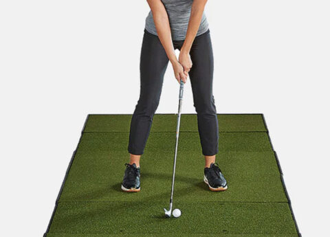 Golfer addressing a golf ball with a wedge on a Fiberbuilt golf mat.